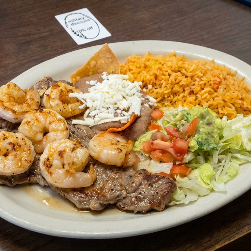 Platter of grilled steak and shrimp with rice, refried beans, guacamole, salad, pico de gallo, and tortilla chips.